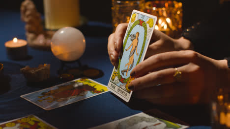 Close-Up-Of-Woman-Giving-Tarot-Card-Reading-On-Candlelit-Table-Holding-The-World-Card-2